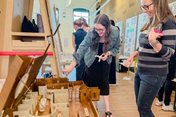 Visitors view a detailed architectural model during a University of Kentucky interiors studio presentation featuring design proposals for The Nest childcare center.