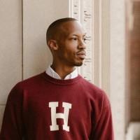 Montreale Jones in a maroon sweater leans casually against a wall, with a relaxed expression on his face.