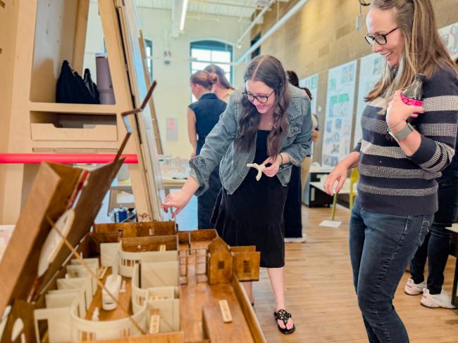 Visitors view a detailed architectural model during a University of Kentucky interiors studio presentation featuring design proposals for The Nest childcare center.