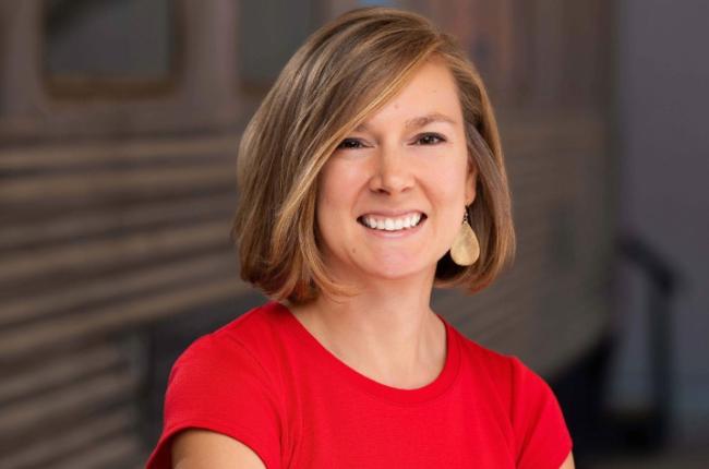 Woman in a red shirt smiles for a professional head shot in front of a blurred background