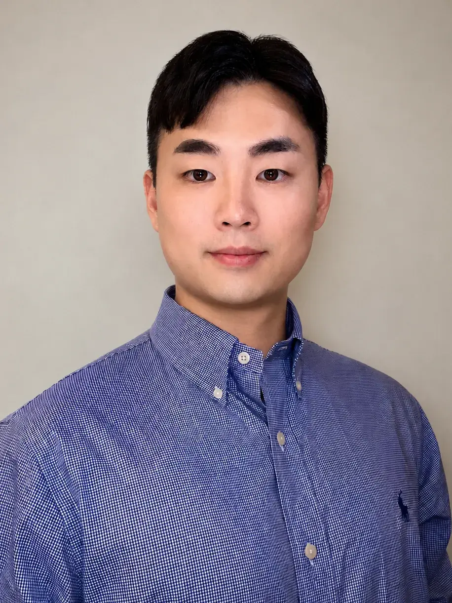 Professional headshot of a young man with short black hair wearing a blue button-down shirt, facing the camera with a calm, neutral expression.